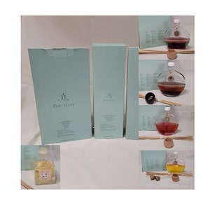 May include: Three boxes of PartyLite scented oil diffusers. The boxes are light blue with white text and a logo of three candles. The diffusers are in glass bottles with a round shape and a cork stopper. The bottles are filled with a clear liquid and have a variety of colours.