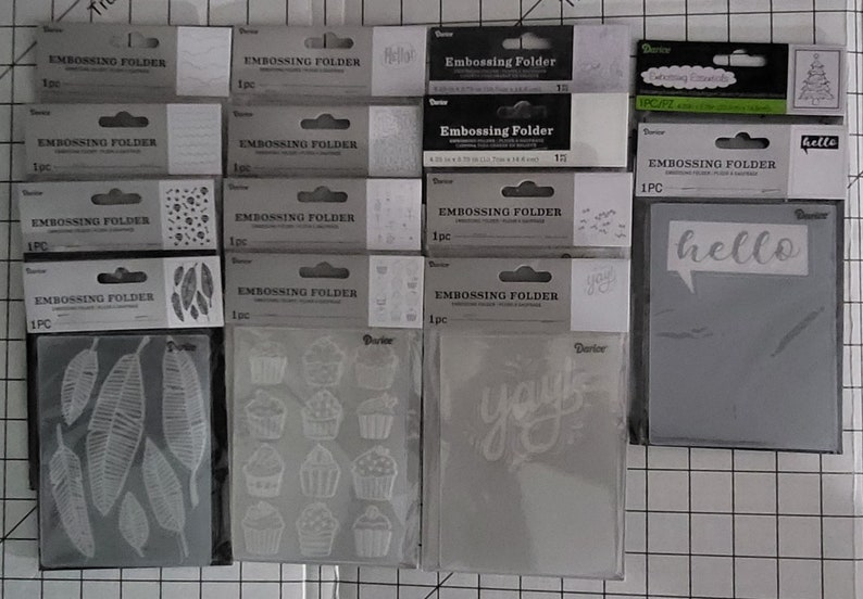 May include: A collection of 12 clear plastic embossing folders with various designs, including leaves, cupcakes, and the words "hello" and "you".