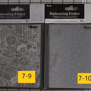 May include: Two clear plastic embossing folders for crafting. The folder on the left has a design of postage stamps and the folder on the right has a design of small dots. The folders are labeled "7-9" and "7-10".
