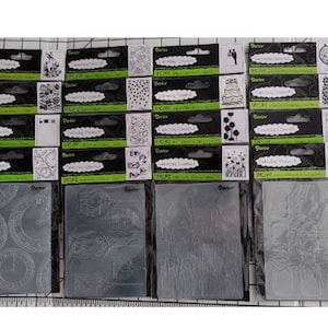 May include: A collection of 18 clear rubber stamps featuring various designs, including clocks, flowers, and buildings. The stamps are packaged in clear plastic sleeves with black and green labels that read "Darice Crafting Essentials".