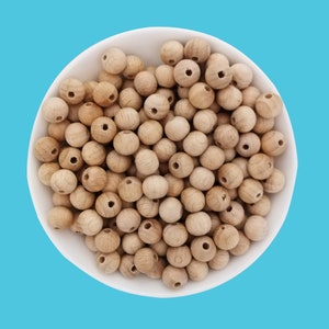 May include: A white bowl filled with natural wood beads. The beads are round and have a hole in the centre. They are a light brown colour.