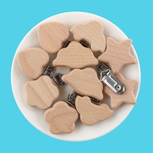 May include: A set of ten wooden baby teethers in various shapes, including hearts, stars, and clouds. Each teether has a silver clip attached.