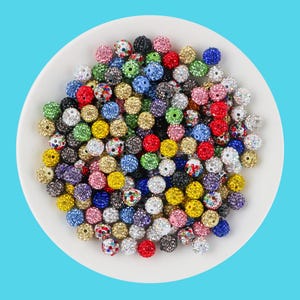 Puede incluir: Una colección de cuentas redondas y coloridas con una superficie brillante y texturizada. Las cuentas son de varios colores, incluyendo rojo, azul, verde, amarillo y rosa, y están dispuestas en un plato blanco sobre un fondo azul. Estas cuentas son ideales para la fabricación de joyas.