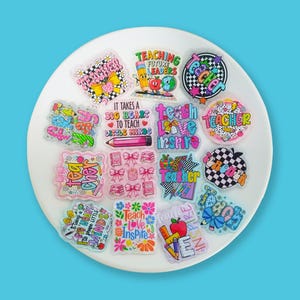 May include: A collection of colorful teacher-themed stickers on a white plate. The stickers feature various designs, including pencils, apples, books, and inspirational quotes like "Teach Love Inspire" and "It Takes a Big Heart to Teach Little Minds."