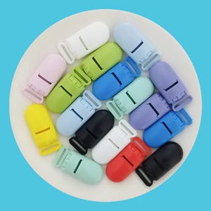 May include: Assortment of colorful plastic clips for attaching pacifiers, teethers, or toys to clothing. The clips come in a variety of colors, including pink, yellow, green, blue, purple, black, and white.