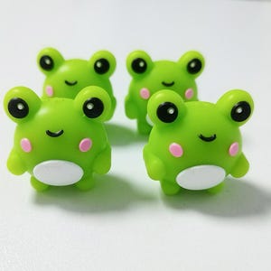 Puede incluir: Cuatro figuritas de rana verde con ojos negros, mejillas rosadas y vientres blancos. Las ranas est&aacute;n hechas de un material suave y gomoso y tienen un aspecto de dibujos animados.