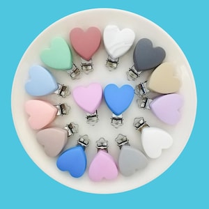 May include: Assortment of 15 silicone heart-shaped teethers with silver clips. The teethers are in various colours, including pink, blue, green, white, and grey.