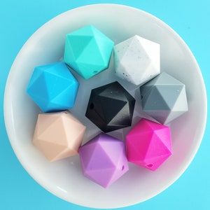 May include: Eight colorful silicone teething beads in various geometric shapes, including turquoise, blue, pink, purple, black, gray, and white.