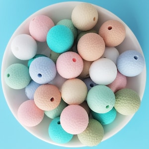 Peut inclure: Un bol rempli de perles en silicone de couleur pastel. Les perles sont rondes et ont une surface texturée. Les perles sont dans différentes nuances de rose, bleu, vert et blanc.