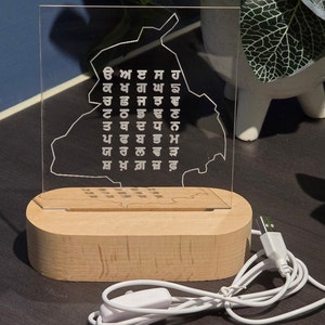 May include: A clear acrylic LED lamp featuring a map outline and text in a stylized font. The lamp sits on a rectangular wooden base and has a USB cable with an on/off switch. The lamp is designed for home decor.
