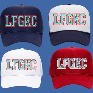 May include: Four trucker hats with a mesh back. The hats are in four different colours: navy blue, white, red, and white. Each hat has the text "LFGK" in a turquoise blue with a red outline.