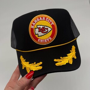 May include: Black trucker hat with a yellow and red Kansas City Chiefs logo and yellow embroidered accents.