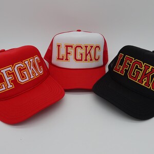May include: Three trucker hats with a red, white and black mesh back. The hats have a white, red and black brim. The front of each hat has the text "LFGKC" in white, red and yellow letters.