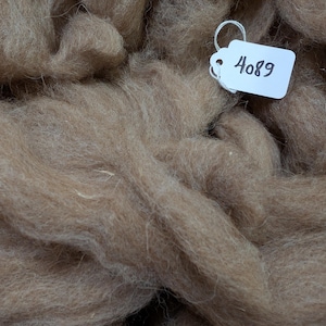 May include: A close-up of a pile of light brown alpaca fiber with a white tag that says "4089".