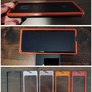 Peut inclure: Cinq étuis de téléphone de différentes couleurs. Les étuis sont en plastique dur et ont une fenêtre transparente au dos. Les couleurs sont noir, blanc, gris, orange et rouge.