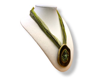 Collier fantaisie vert en tissu retenant un imposant pendentif métallique incrusté de motifs en résine