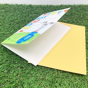 May include: A folded card with a yellow envelope. The card has a drawing of a golf bag with clubs and the text "Best Dad By Par". The card has a blue, green, yellow, red, and white colour scheme.