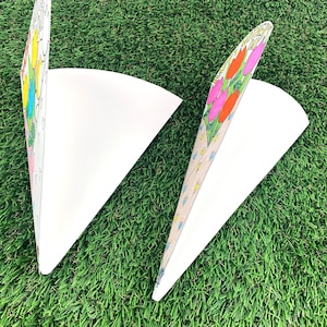 May include: Two white paper cones with colorful flower designs. The cones are folded and ready to be filled with treats or gifts.