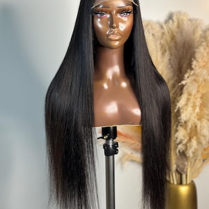 May include: A long, straight, jet-black wig displayed on a mannequin head. The wig features a center part and a sheer lace front hairline that sits across the forehead. The hair is smooth, sleek, and extends past the shoulders in a uniform length.