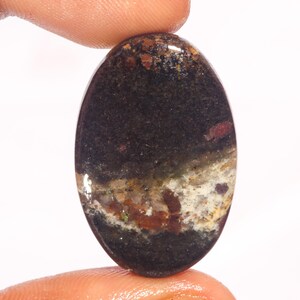 以下が含まれることがあります： 黒、白、茶色の模様が施された楕円形のcabochonカットの宝石。石は半透明で、色とテクスチャが混ざり合っています。