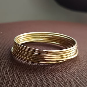 May include: A set of seven gold-coloured metal bangles stacked on top of each other. The bangles are smooth and shiny.