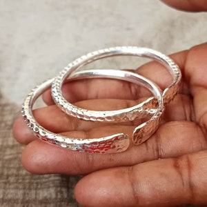 May include: Two silver hammered bangle bracelets. The bracelets are open ended and have a textured surface.