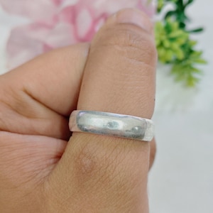 Könnte beinhalten: Ein schlichter, glatter Bandring in Silberoptik mit polierter Oberfläche. Der Ring weist ein gleichmäßiges, abgerundetes Profil und eine schlichte, verzierungsfreie Oberfläche auf, die den Finger umschließt und ein klares, metallisches Aussehen bietet.
