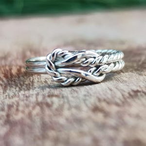 Puede incluir: Un anillo de plata con un diseño de nudo trenzado. El anillo está hecho de dos bandas de plata que se entrelazan para crear un nudo.
