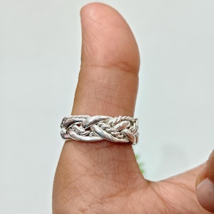 May include: A silver ring featuring a complex, multi-strand braided design. The band is constructed from several intertwined metallic strands that create a textured, woven appearance with polished highlights and shadowed recesses throughout the metal.