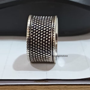 May include: A silver ring with a textured design. The ring is wide and has a rounded shape.