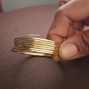 May include: A stack of eight gold-coloured bangles. The bangles are smooth and shiny.