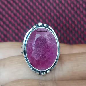May include: A silver ring with a large, oval-shaped, pink gemstone set in a bezel setting. The ring has a textured band and a decorative border around the gemstone.