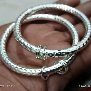 May include: Two silver bangles with a hammered texture. The bangles are connected by a silver wire.