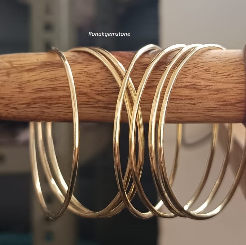 May include: A set of seven gold-toned bangle bracelets. The bracelets are stacked on top of each other and are arranged in a circular pattern.