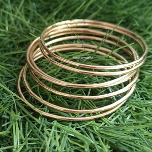 May include: A set of seven gold-toned bangle bracelets. The bracelets are stacked on top of each other and are arranged in a circular pattern. The bracelets are smooth and shiny.