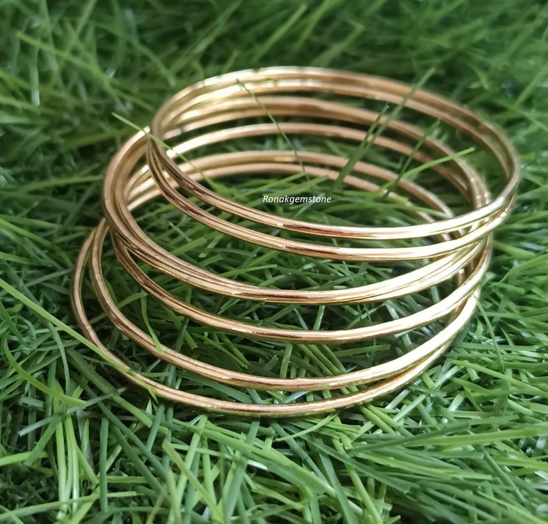May include: A set of seven gold-toned bangle bracelets. The bracelets are stacked on top of each other and are arranged in a circular pattern. The bracelets are smooth and shiny.