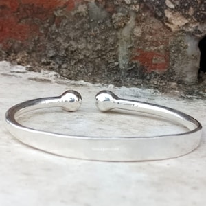 May include: A silver bangle bracelet with rounded ends. The bracelet is smooth and has a polished finish.