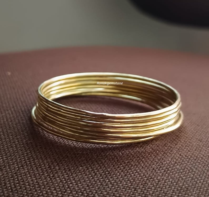 May include: A set of seven gold-coloured metal bangles stacked on top of each other. The bangles are smooth and shiny.
