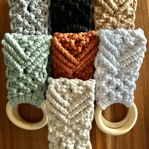 May include: A set of eight macrame rings with wooden rings. The rings are in various colours, including grey, black, beige, green, orange, and white.