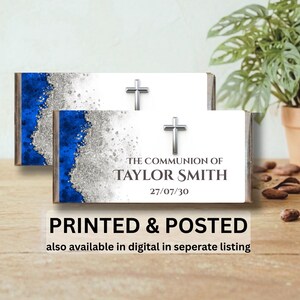 May include: Two rectangular chocolate bar wrappers featuring a white background with a blue and silver glitter-effect border. Each wrapper displays a silver cross and the text THE COMMUNION OF TAYLOR SMITH 27/07/30 in dark grey lettering.