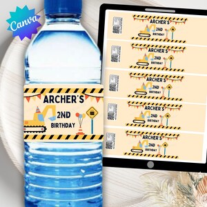 Op de afbeelding: Een waterfles met een label met de tekst "ARCHER'S 2ND BIRTHDAY" met een gele bouwmachine-afbeelding. Extra labels met hetzelfde ontwerp zijn zichtbaar op een tablet.