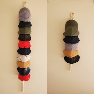 May include: A collection of nine baseball caps hanging on a wall rack. The caps are in various colours, including black, red, blue, green, and yellow. The caps are arranged in a vertical stack, with the top cap being a grey cap.
