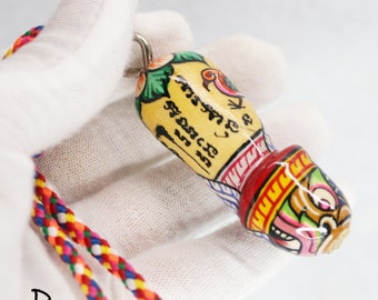 May include: A colorful wooden pendant with a painted design of a bird and text in a foreign language. The pendant is attached to a multi-colored cord.