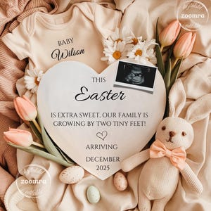 May include: A heart-shaped sign with the text "This Easter is extra sweet, our family is growing by two tiny feet!"  The sign is surrounded by pastel pink and white flowers, a baby onesie, a stuffed bunny, and Easter eggs. The text "Baby Wilson Arriving December 2025" is also on the sign.