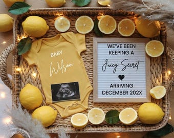 May include: A yellow baby onesie with the name "Wilson" and an ultrasound image, surrounded by lemons and lemon slices in a woven basket. A letter board reads "We've been keeping a juicy secret arriving December 202X."