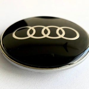 May include: A black and silver car emblem with four interlocking rings.
