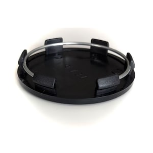 Op de afbeelding: Zwarte kunststof wielnaafdop met een zilveren metalen ring rond de rand. De dop heeft zes lipjes die in het wiel passen.