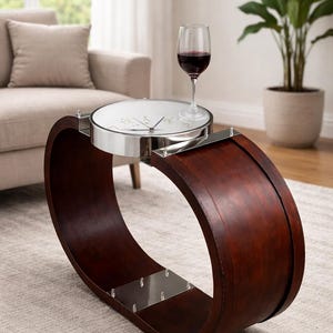 Op de afbeelding: Een unieke, donkerbruine, gebogen salontafel met een klokvormig blad en een roestvrijstalen rand. Een glas rode wijn staat op de tafel. De tafel staat op een lichtgekleurd tapijt in een woonkamer.
