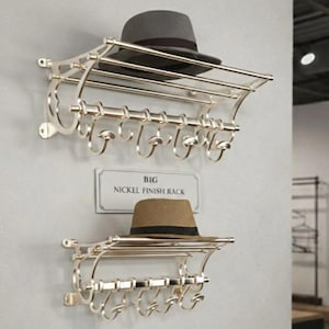 May include: Two nickel finish hat racks on a grey wall. A grey fedora sits on the top rack, and a brown fedora on the bottom. The top rack is labelled "BIG NICKEL FINISH RACK". The bottom rack is labelled "SMALL NICKEL FINISH RACK".