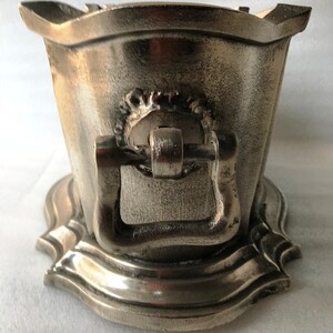May include: A silver metal ice bucket with a decorative handle and a scalloped base.